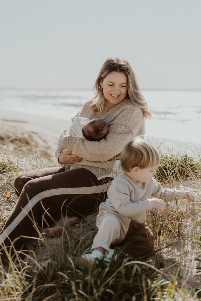 woman holding her baby and looking at her son at the beach what to wear to family beach session 