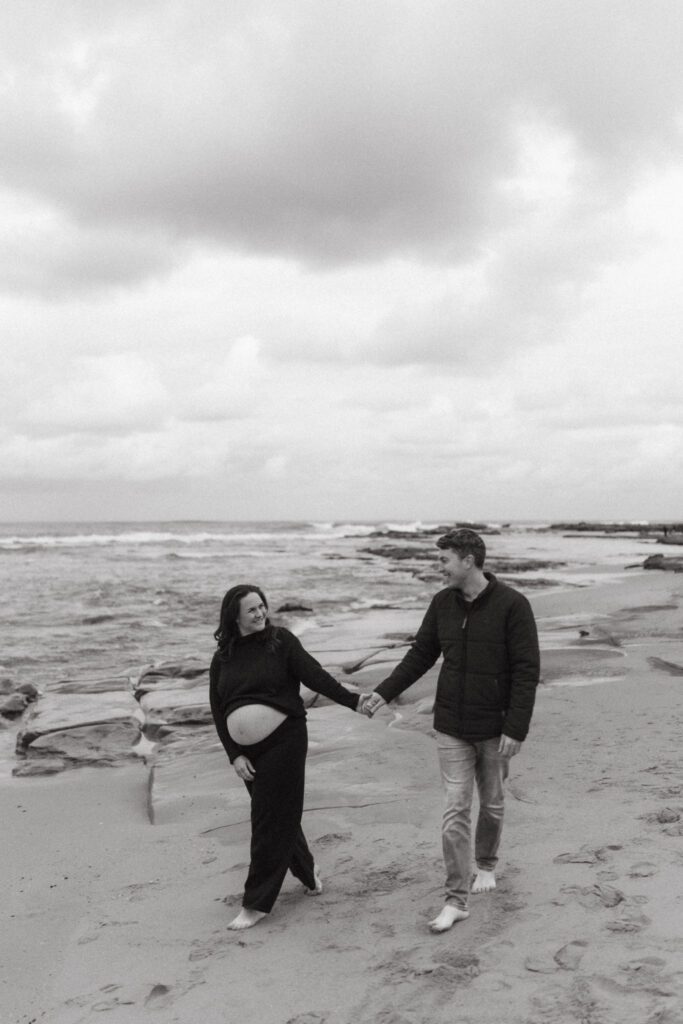 pregnant woman and man walking along the beach  showing you can wear black to your family photos